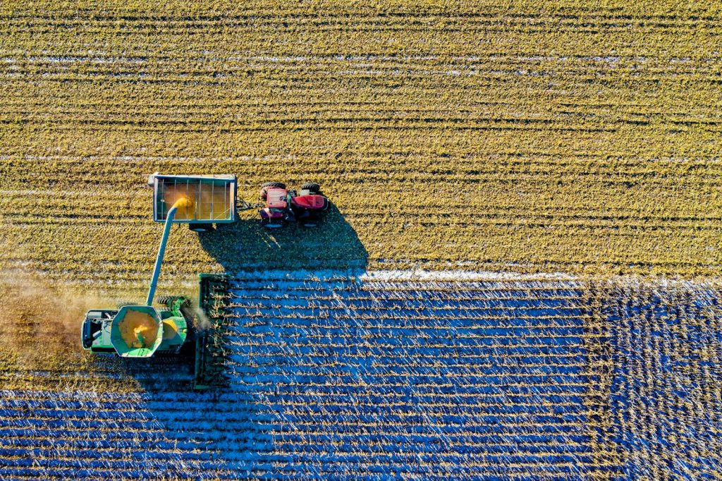 Drone captures vibrant aerial view of tractors harvesting corn in Minnesota field.